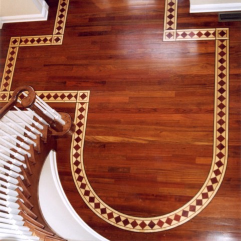 Warm hardwood floor with custom geometric wood border inlay beside a curved staircase