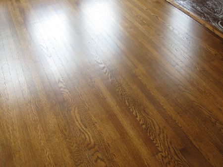 Freshly refinished honey-stained oak floor with rich grain figure beside a patterned rug edge in a historic Houston home