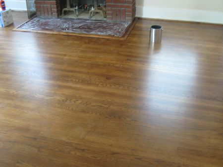 Wood floor sanding and finishing in a Houston living room Freshly sanded and finished medium-brown oak floor with a glossy sheen beside a brick fireplace in Houston