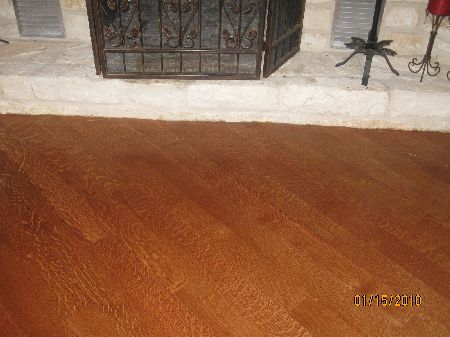 Amber quartersawn white oak floor showing distinctive ray-fleck grain in front of a stone fireplace hearth