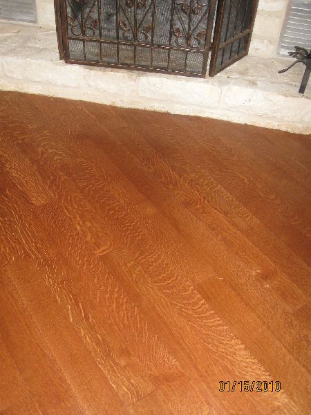 Golden amber quartersawn white oak floor showing tight straight grain and ray-fleck figure by a stone fireplace in Houston